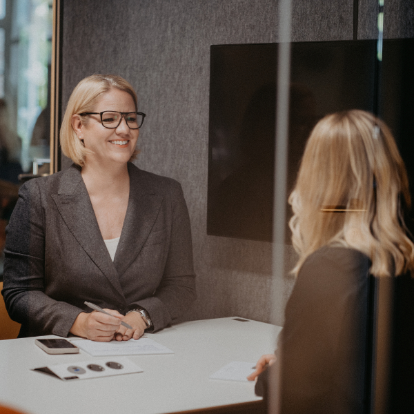 Zwei Frauen, die sich, mit einem Tisch dazwischen im Coaching-Gespräch befinden.